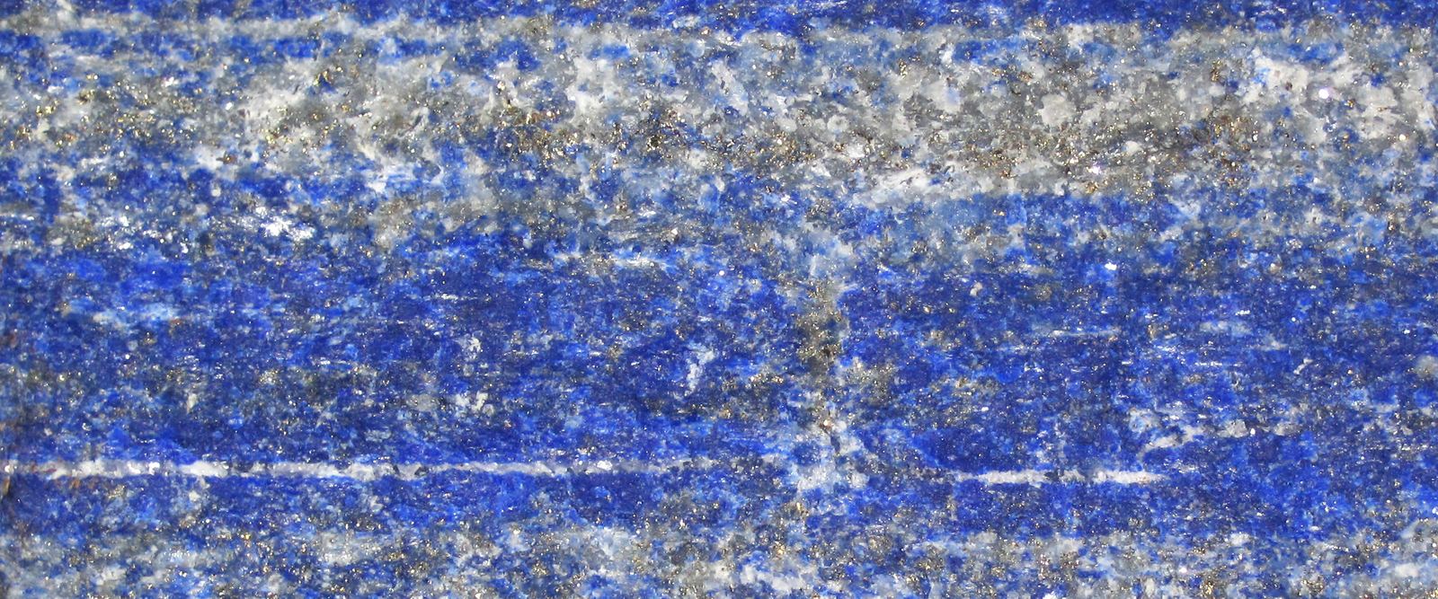 Raw lapis lazuli from Sar-e-Sang, Afghanistan: deep blue stone in layers, with thin white bands and grey flecks running across it.